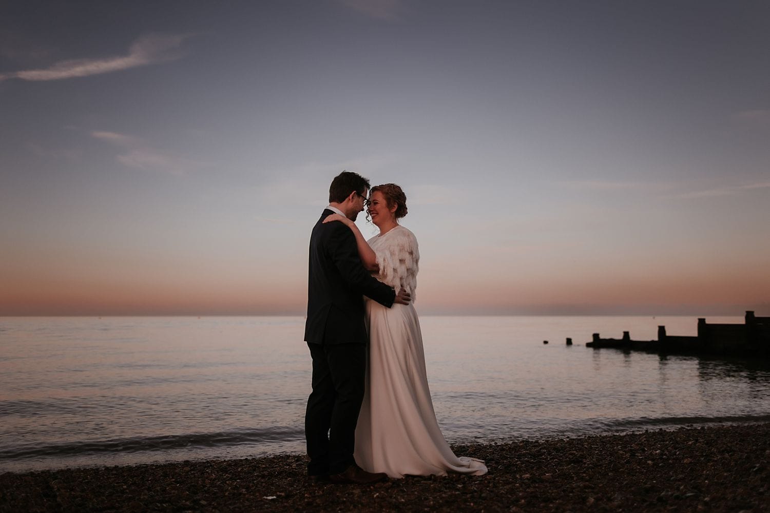 Bride and Groom on Whitstable beach at East Quay holding hands at sunset
