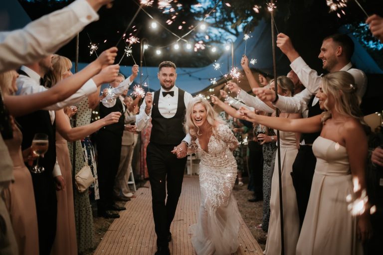 Bride and groom walking through a tunnel of sparklers, the bride is laughing