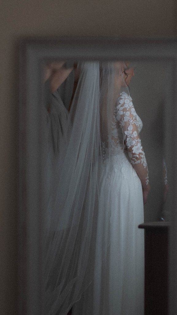 Brides refelection in a mirror as she has her veil adjusted by her mum